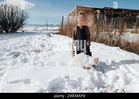 la bambina di 4 anni ama giocare sulla neve all'aperto con il suo gatto bianco e soffice Foto Stock