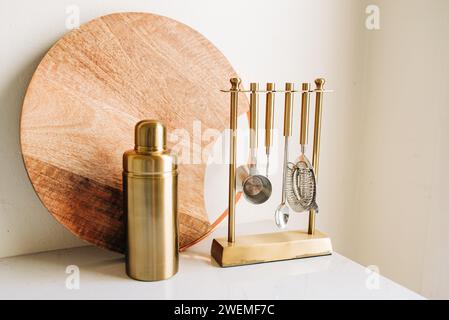 Tagliere in legno e set di miscelazione cocktail oro su contatore bianco Foto Stock