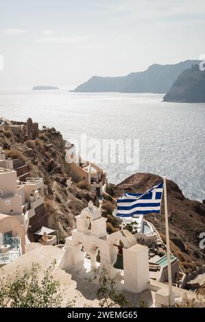 Bandiera greca e campane della chiesa che si affacciano sul villaggio di Oia Foto Stock