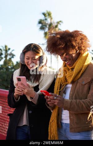 Giovani coppie multirazziali si sono riunite all'aperto usando i telefoni cellulari allegramente. Foto Stock