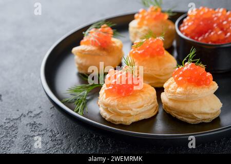 Toast al caviale rosso salmone. Canape natalizia o brindisi con caviale rosso su piatto nero su sfondo scuro. Un'idea per uno spuntino di Natale. Cibo da buongustai. Trama della cav Foto Stock