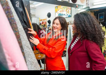 Amici che guardano abiti dall'appendiabiti di un negozio di seconda mano durante le vendite Foto Stock