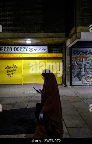 Donna musulmana in velo che cammina lungo la East London Street guardando il suo telefono Foto Stock