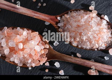 Due cucchiai di legno adagiati su un'ardesia sono riempiti di sale rosa Foto Stock