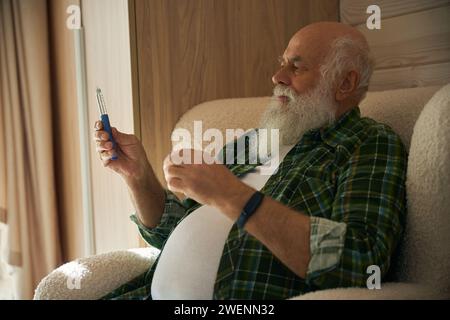 Il pensionato in una camicia a scacchi tiene il termometro in mano Foto Stock