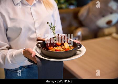 La cameriera serve gambo di agnello, guarnito con un rametto di timo Foto Stock