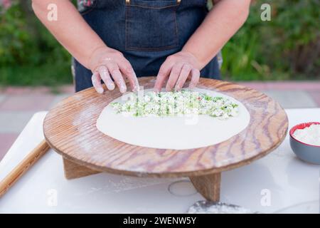 Vecchia cuoca, chef che indossa la pita per preparare il grembiule e ripieno di formaggio sull'impasto. Foto Stock