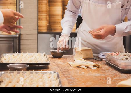 Primo piano sulla preparazione del cibo presso la cucina di un ristorante cinese mentre il personale assembla gnocchi dim sum a Taipei, Taiwan. Foto Stock