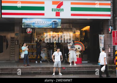 Taipei, Taiwan - 1° ottobre 2023: Gente urbana vivace e colorata e scene di strada davanti a 7-11 minimarket e mascotte Open-Chan nel trambusto Foto Stock