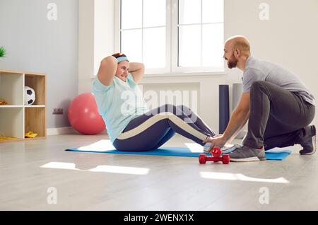 Giovane infermiera amichevole maschile che aiuta la donna grassa in sovrappeso che fa esercizi sportivi Foto Stock