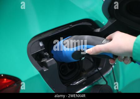 Erfurt, Germania. 26 gennaio 2024. Un dipendente della Stadtwerke Erfurt collega un cavo di ricarica alla presa di un'auto elettrica in una sala espositiva dell'Automobil Messe Erfurt. Un totale di 130 espositori presenta gli ultimi sviluppi nel mercato automobilistico in tre sale espositive. Credito: Bodo Schackow/dpa/Alamy Live News Foto Stock