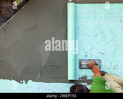 Posare con cazzuola un tappetino fonoassorbente sul rasatore. Foto Stock