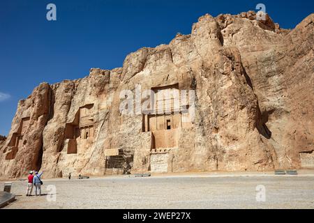 I turisti guardano le tombe scavate nella roccia dei re persiani della dinastia achemenide nella Necropoli di Naqsh-e Rostam vicino a Persepoli, in Iran. Foto Stock