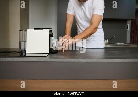 Foto ritagliata di un uomo irriconoscibile che prepara il caffè a casa con una macchina da caffè elettrica. Foto Stock