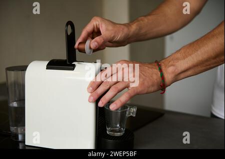 Il primo piano maschio prepara il caffè espresso per la colazione al mattino, inserendo una capsula con arabica macinato all'interno di una macchina per il caffè a capsule per Foto Stock