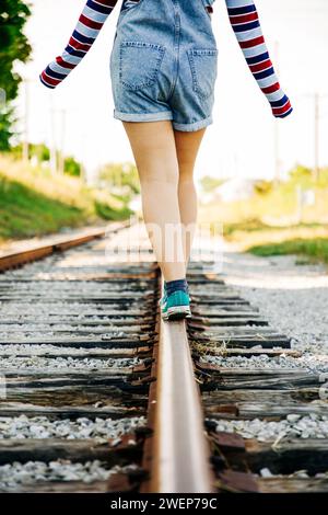 Una donna con le zampe piccole passeggia lungo i binari del treno, crogiolandosi nel calore di una giornata di sole Foto Stock