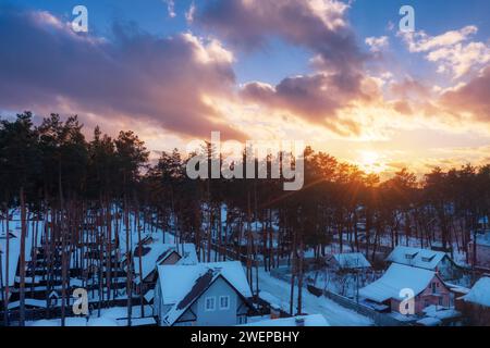 Tramonto bellissimo la sera d'inverno sulle case con tetti innevati fuori città. Foto Stock
