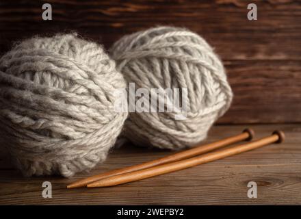 Palle di filato di lana grigio e aghi per maglieria su fondo di legno. Concetto di fatto a mano. Foto Stock