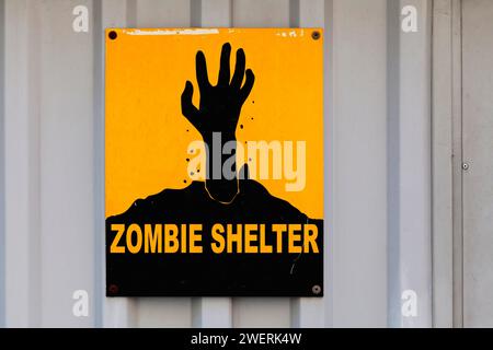 Mano nera che si solleva da terra disegnata su un cartello giallo con scritto "Zombie Shelter". Foto Stock