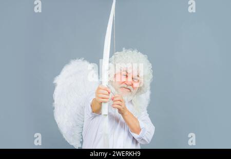 San Valentino. Uomo barbato sorridente in costume d'angelo che mira con l'arco. Angelo di San Valentino maschio in parrucca bianca sparano freccia d'amore. San Valentino cupid in Foto Stock