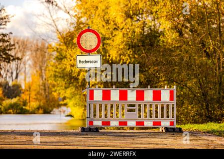 Atmosfera retroilluminata al sole con segnale di avvertimento acqua alta su una strada sul Reno, Germania Foto Stock