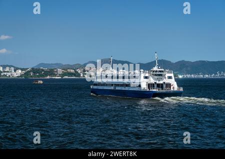 Il traghetto Neves V naviga sulle acque della baia di Guanabara verso la stazione terminale di Arariboia nel quartiere Centro di Niteroi sotto il cielo blu pomeridiano estivo. Foto Stock