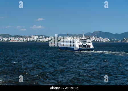 Il traghetto Neves V naviga sulle acque della baia di Guanabara verso la stazione terminale di Arariboia nel quartiere Centro di Niteroi sotto il cielo blu pomeridiano estivo. Foto Stock