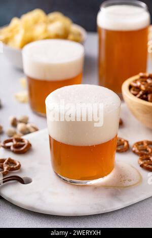 Birra lager in bicchieri con una varietà di spuntini, pretzel, patatine fritte e pistacchi Foto Stock