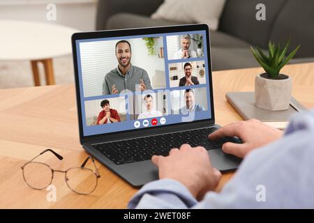 Uomo che ha videochiacchierato con i colleghi tramite un computer portatile al tavolo di legno, primo piano Foto Stock