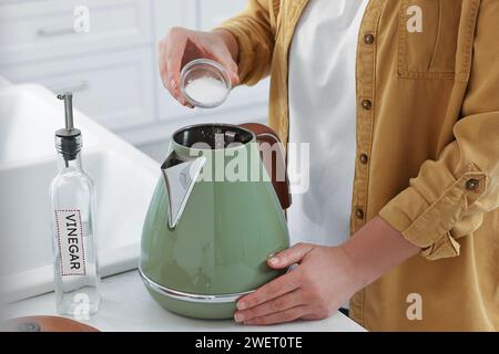Donna che aggiunge bicarbonato di sodio nel bollitore elettrico in cucina, primo piano Foto Stock