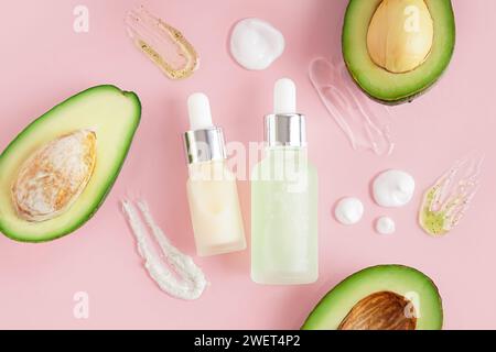 Composizione con avocado fresco tagliato, bottiglie di olio essenziale e campioni su fondo rosa Foto Stock