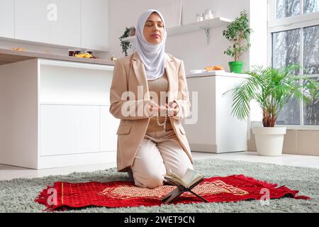 Giovane donna musulmana che prega con perline in cucina. Festa del Ramadan Foto Stock