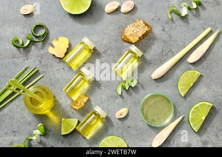 Bottiglie di oli essenziali e piastra Petri su sfondo grigio. Erbe fresche - limone, scorza di limone, citronella e zenzero. Buono per la salute, la cura della pelle e i capelli Foto Stock