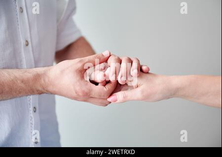 Primo piano di due mani con un tocco delicato. Mani di uomini e donne su sfondo bianco neutro. Marito che tiene per mano la sua adorabile moglie. Concetto di amore, intimità, sostegno e fiducia. Foto Stock