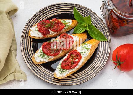 Diversi panini pronti con pomodori secchi, formaggio e aneto in un piatto di ceramica con menta sul tavolo, vista dall'alto Foto Stock