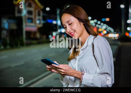 la donna si trova sul lato di una strada di notte, tenendo il cellulare e cercando di cavalcare Foto Stock