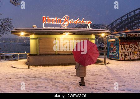 Donna con ombrello in piedi di fronte a un chiosco chiuso sulla passeggiata innevata sul Reno vicino al ponte Hohenzollern, Snow, Colonia, Germania. 17.01.2024 Frau Foto Stock