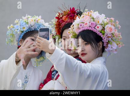 (240127) -- QUANZHOU, 27 gennaio 2024 (Xinhua) -- i turisti che indossano copricapo fiorito fanno selfie al villaggio di Xunpu della città di Quanzhou, provincia del Fujian della Cina sudorientale, 26 gennaio 2024. I copricapo fioriti Xunpu, soprannominati "giardini sopraelevati", sono stati una firma della "Xunpu Women Customs" elencata come patrimonio immateriale nazionale nel 2008. Hanno attirato milioni di occhi nel mondo cyber all'inizio del 2023, seguito da un boom turistico sostenibile nel villaggio, dove i visitatori sono in grado di mettere letteralmente la testa in loro. Servizi fotografici, gastronomici e altri servizi alberghieri hanno diversificato la fonte di inco Foto Stock