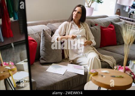 La donna incinta felice è seduta sul divano con una tazza di caffè Foto Stock