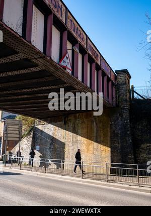 Il sole splende attraverso un ponte ferroviario basso che attraversa Brighton Road con un uomo che cammina sotto a Redhill nel Surrey in Inghilterra Foto Stock