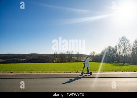 Sonnige e-Scooter-Tour durch die winterliche Landschaft ohne Schnee 27.01.2024, Selters: Symbolfoto, Illustrationsbild, Symbolbild, Illustrationsfoto Sonnige e-Scooter-Tour durch die winterliche Landschaft ohne Schnee Eine Frau in winterlicher Kleidung genießt eine sonnige Fahrt auf einem e-Scooter entlanes eines. Trotz der winterlichen Jahreszeit liegt kein Schnee stattdessen bieten die umliegenden Felder und Wiesen eine malerische Kulisse. Selters Hessen Germania *** Tour soleggiato in e-scooter attraverso il paesaggio invernale senza neve 27 01 2024, foto simbolo Selters, immagine illustrazione, SY Foto Stock