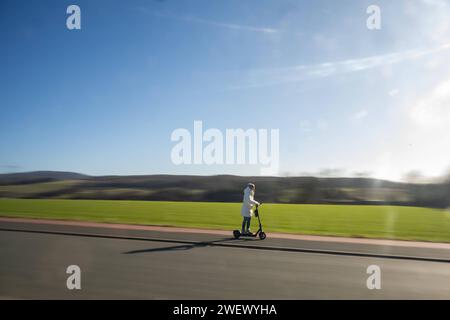 Sonnige e-Scooter-Tour durch die winterliche Landschaft ohne Schnee 27.01.2024, Selters: Symbolfoto, Illustrationsbild, Symbolbild, Illustrationsfoto Sonnige e-Scooter-Tour durch die winterliche Landschaft ohne Schnee Eine Frau in winterlicher Kleidung genießt eine sonnige Fahrt auf einem e-Scooter entlanes eines. Trotz der winterlichen Jahreszeit liegt kein Schnee stattdessen bieten die umliegenden Felder und Wiesen eine malerische Kulisse. Selters Hessen Germania *** Tour soleggiato in e-scooter attraverso il paesaggio invernale senza neve 27 01 2024, foto simbolo Selters, immagine illustrazione, SY Foto Stock