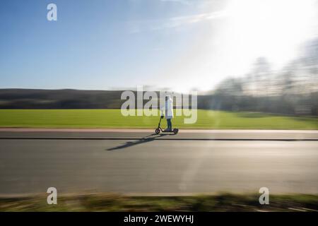 Sonnige e-Scooter-Tour durch die winterliche Landschaft ohne Schnee 27.01.2024, Selters: Symbolfoto, Illustrationsbild, Symbolbild, Illustrationsfoto Sonnige e-Scooter-Tour durch die winterliche Landschaft ohne Schnee Eine Frau in winterlicher Kleidung genießt eine sonnige Fahrt auf einem e-Scooter entlanes eines. Trotz der winterlichen Jahreszeit liegt kein Schnee stattdessen bieten die umliegenden Felder und Wiesen eine malerische Kulisse. Selters Hessen Germania *** Tour soleggiato in e-scooter attraverso il paesaggio invernale senza neve 27 01 2024, foto simbolo Selters, immagine illustrazione, SY Foto Stock