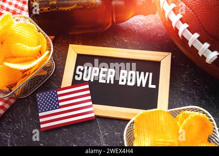 Germania - 27 gennaio 2024: Scritta del Super Bowl su una tavola circondata da spuntini, birra e football americano per il Super Bowl insieme a una bandiera degli Stati Uniti. Evento sportivo in America FOTOMONTAGGIO *** Super Bowl Schriftzug auf einer Tafel umgeben von Snacks, Bier und ein American Football zum Super-Bowl zusammen mit einer USA Fahne. Sportveranstaltung in Amerika FOTOMONTAGE Foto Stock