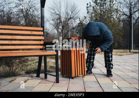 Un vecchio uomo caucasico senzatetto ruba per cibo e spazzatura in un cestino in autunno in un parco Foto Stock