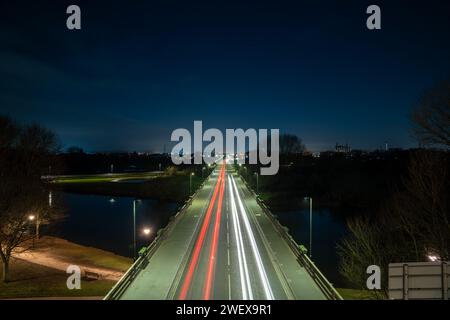 Lunghe piste luminose per auto che passano attraverso un ponte in una piccola città durante la notte Foto Stock