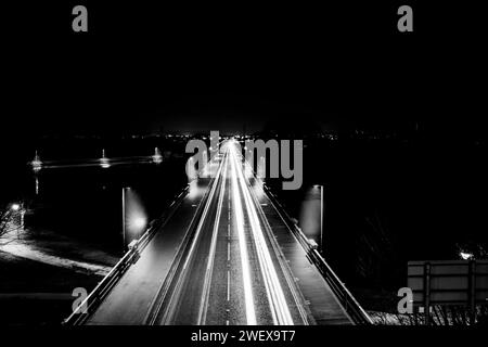 Lunghe piste luminose per auto che passano attraverso un ponte in una piccola città durante la notte Foto Stock