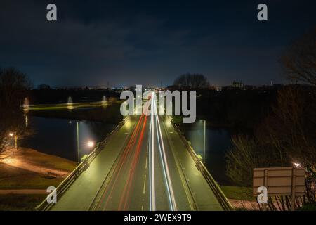 Lunghe piste luminose per auto che passano attraverso un ponte in una piccola città durante la notte Foto Stock