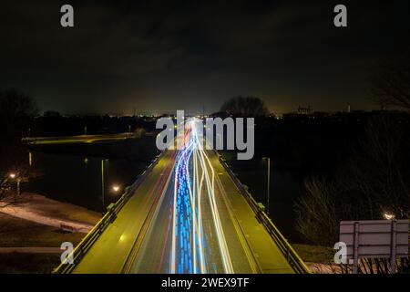 Lunghe piste luminose per auto che passano attraverso un ponte in una piccola città durante la notte Foto Stock