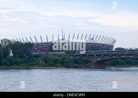 Varsavia, Polonia - 8 giugno 2019: Treni che attraversano il ponte di Średnicowy sul fiume Vistola con alle spalle lo Stadio Nazionale. Foto Stock